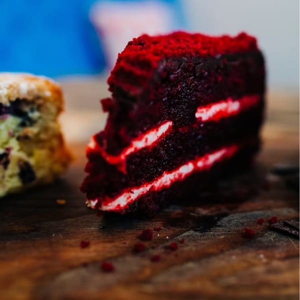 A slice of red velvet cake with white frosting layers sits next to a blueberry scone.