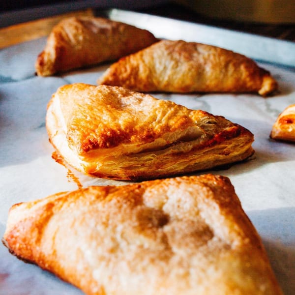 Golden brown, flaky Mexican empanadas or pastries arranged on a baking sheet.
