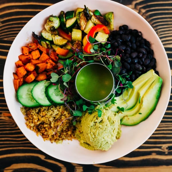 A colorful Chula Artisan Eatery vegan bowl with roasted vegetables, black beans, avocado, and green sauce.