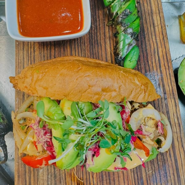 Chula Artisan Eatery's Mexican torta with avocado, onions, and greens, served with red sauce.