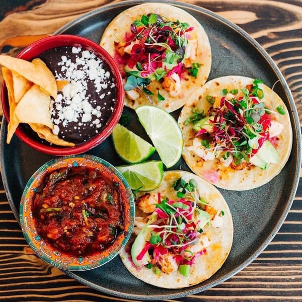 Three Chula Artisan Eatery tacos with sides of black beans, salsa, and lime wedges.