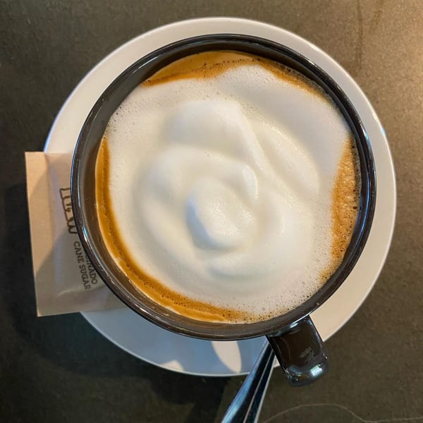 Overhead view of a Chula Artisan Eatery cappuccino with thick foam, on a white saucer.