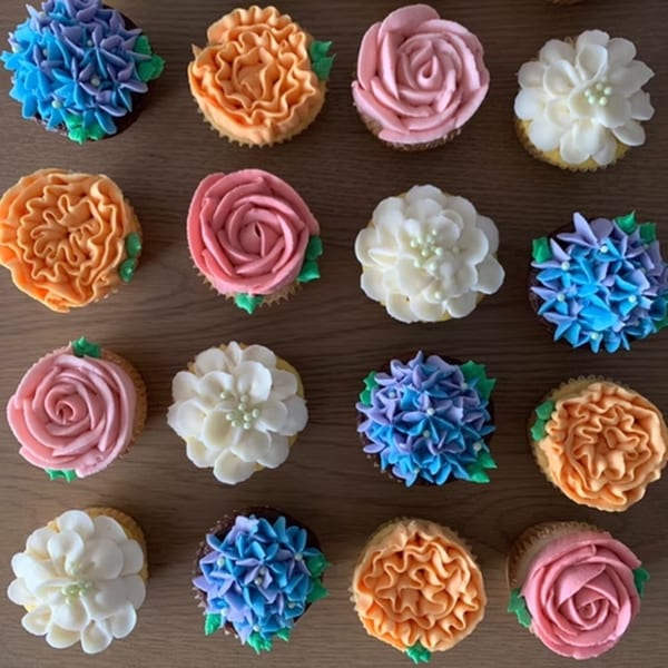 Overhead view of sixteen cupcakes with colorful floral frosting designs on a wooden surface.