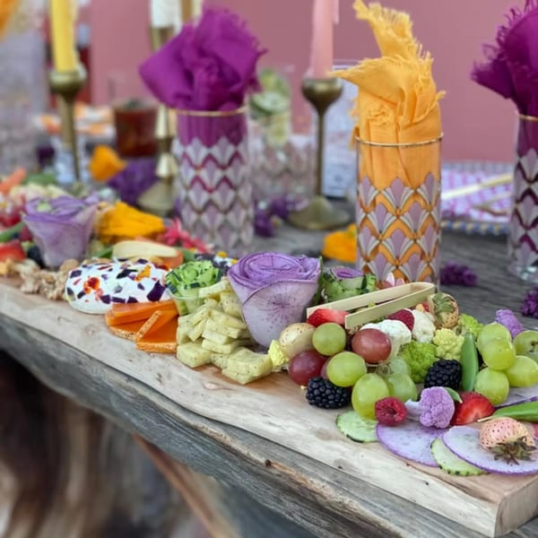 A vibrant charcuterie board with cheeses, fruits, and vegetables, set on a rustic wooden table.