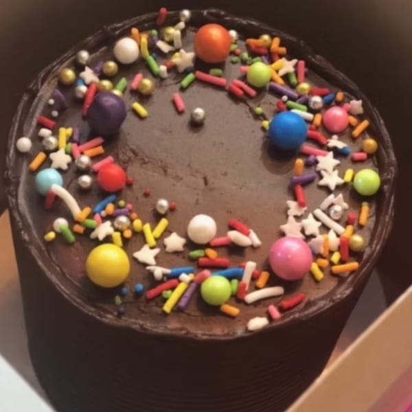Chocolate cake with colorful sprinkles, candy pearls, and star-shaped candies on top.